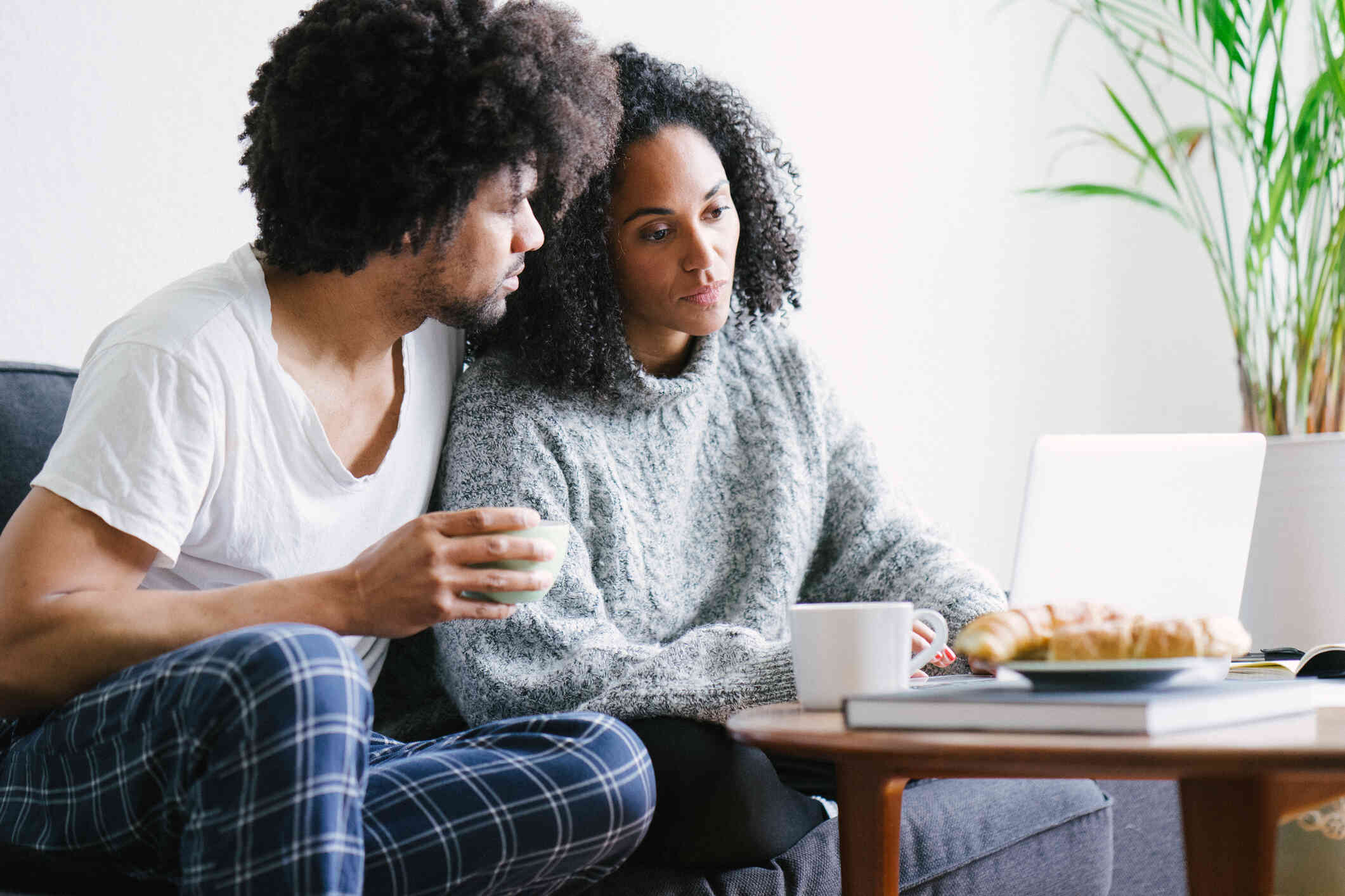 A woman looks sad while looking at her laptop while the man try to sit closely, offering comfort.